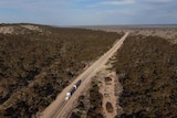 An aerial view of a truck on a highway, driving through arid bushland.