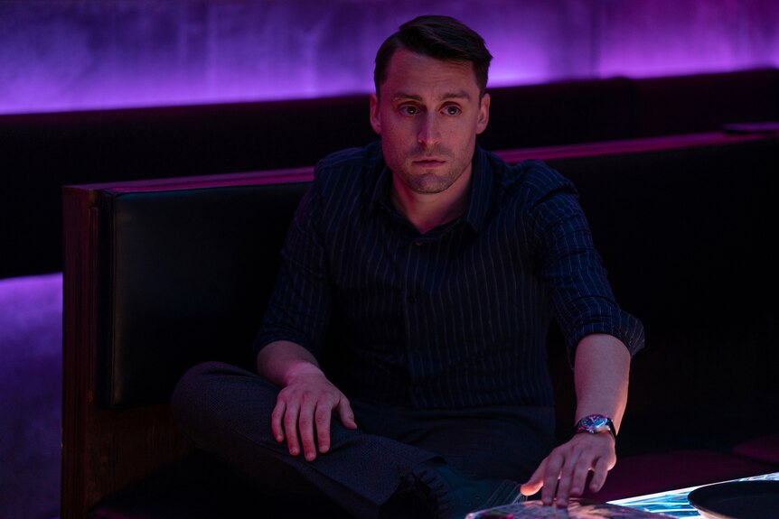 Roman sits in a karaoke bar with purple lighting.