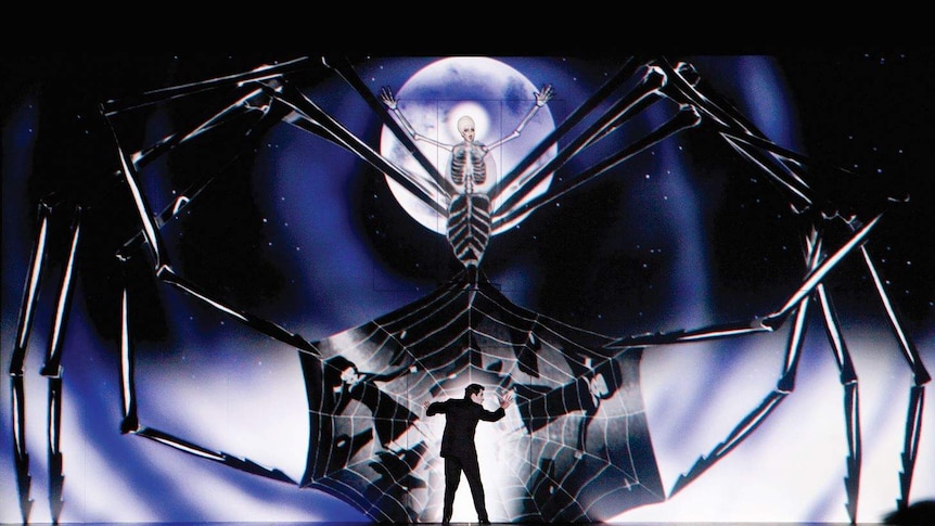 A stage filled with a projection of an enormous spider, a woman is the spider and a man is in her web