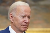 An emotional Joe Biden looks away from the cameras with a blurred painting behind him in the White House.