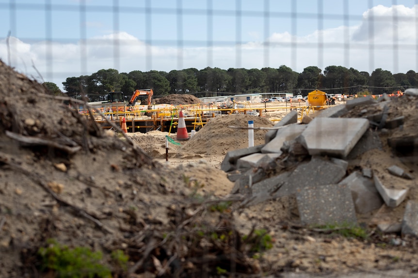 A sandy, fenced off construction site full of rubble.