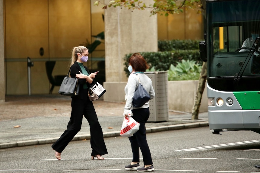 Deux femmes portant des masques traversent une route dans le CBD de Perth avec un bus en arrière-plan.