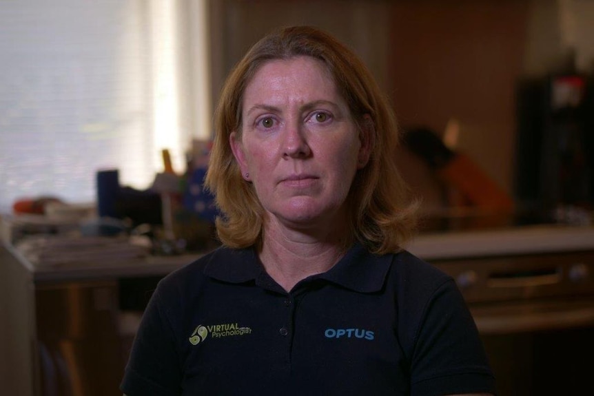 Woman in polo shirt looks serious, sitting inside home.