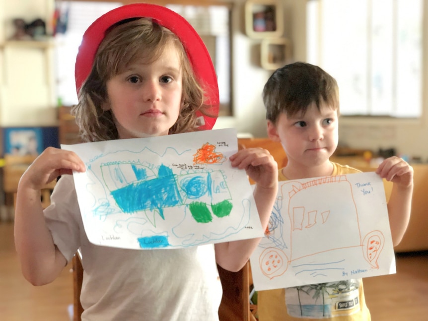 Two kindergarten-aged boys hold drawings of fire trucks.