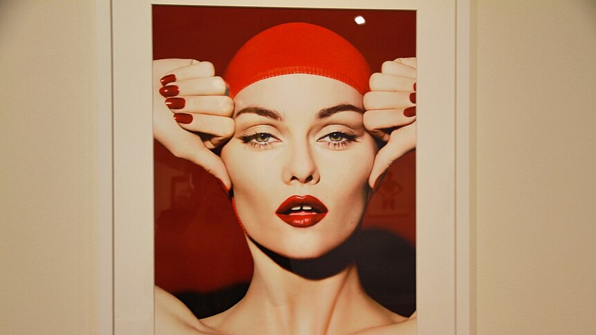 A framed image of woman wearing a red cap and red lipstick looking straight into camera.
