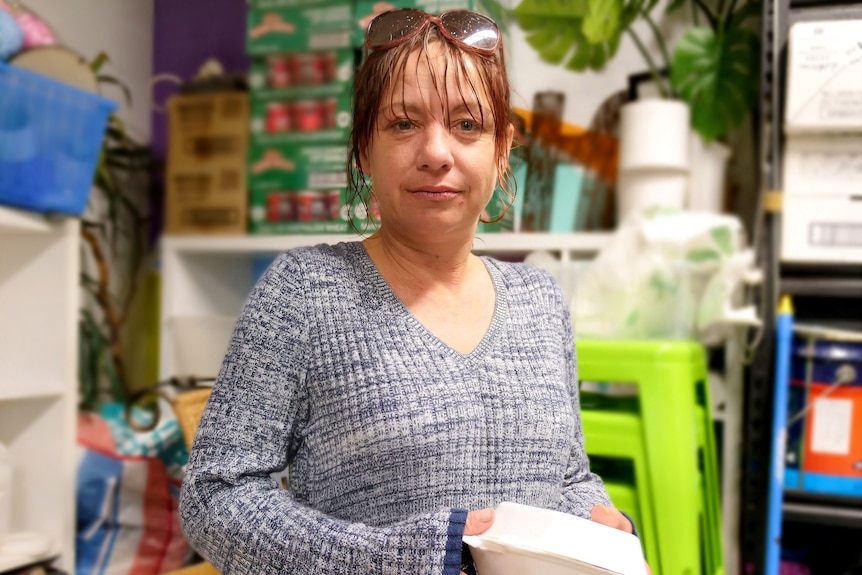 A woman stands in front of a stockpile of food and essentials at a homeless shelter