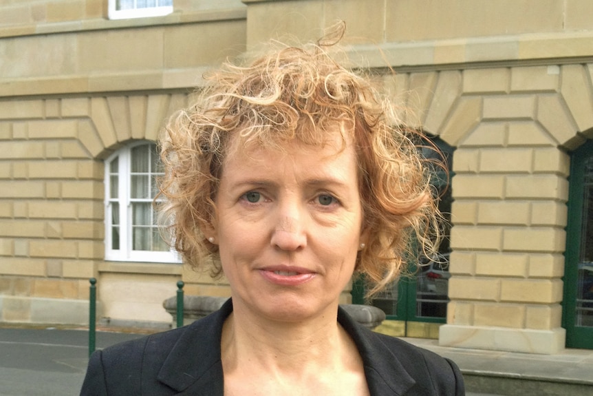 Ruth Forrest stands in front of a building, looking into the camera.