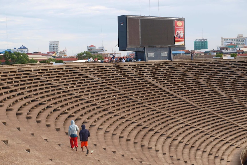 Two figures walk across curving empty stadium seating