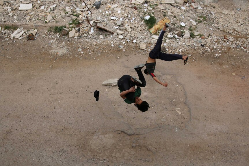 Two Syrian men perform parkour moves on the rubble-strewn streets of the Syrian city of Inkhil.