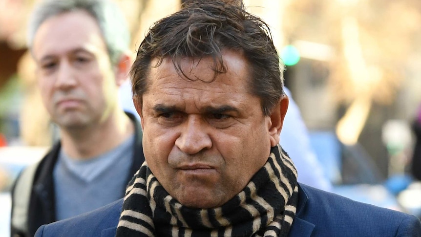Nicky Winmar walks to court wearing a blue suit and brown striped scarf.