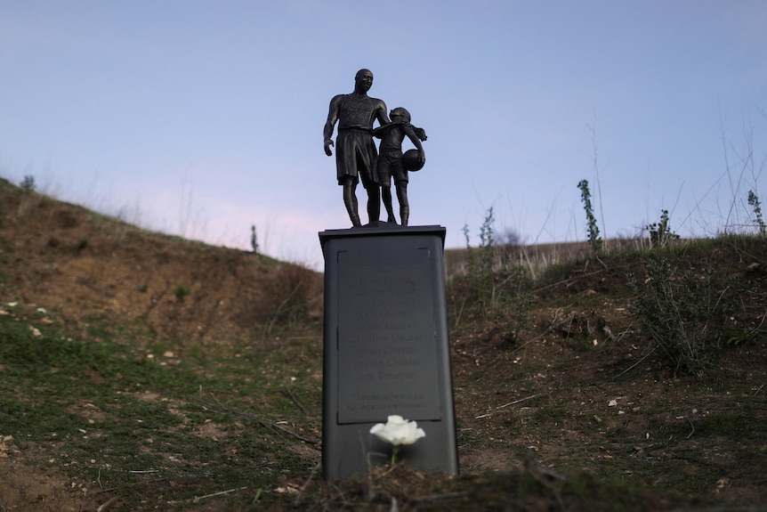 A sculpture of a man and a young girl holding a basketball on a hillside as the sun sets.