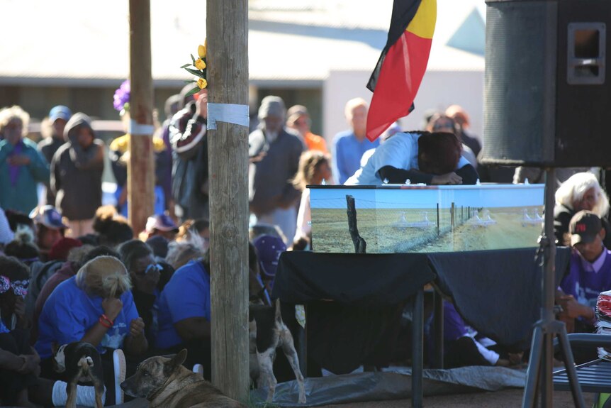 Mourners surround Daisy Kadibil's coffin. Her coffin is painted with the rabbit-proof fence.