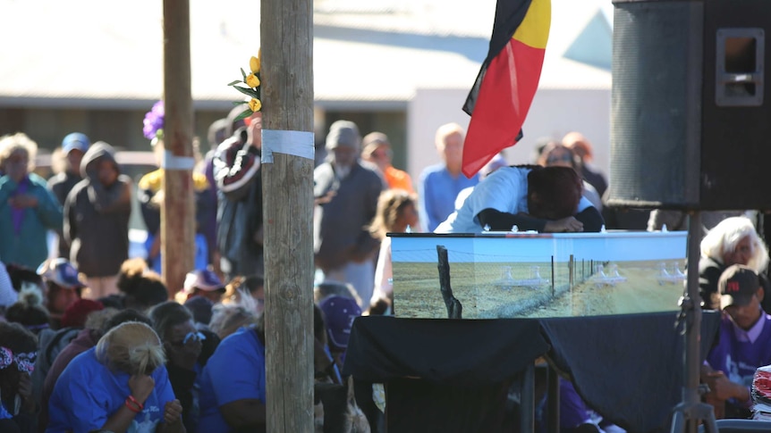 Mourners surround Daisy Kadibil's coffin. Her coffin is painted with the rabbit-proof fence.