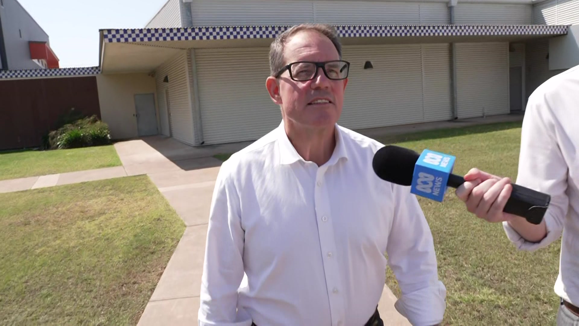 Luke Gosling walking out of a police station in a white button up shirt, with an ABC microphone in front of him held by person.