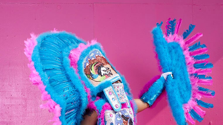 A man adorned in a striking and brightly-coloured blue and pink ceremonial costume
