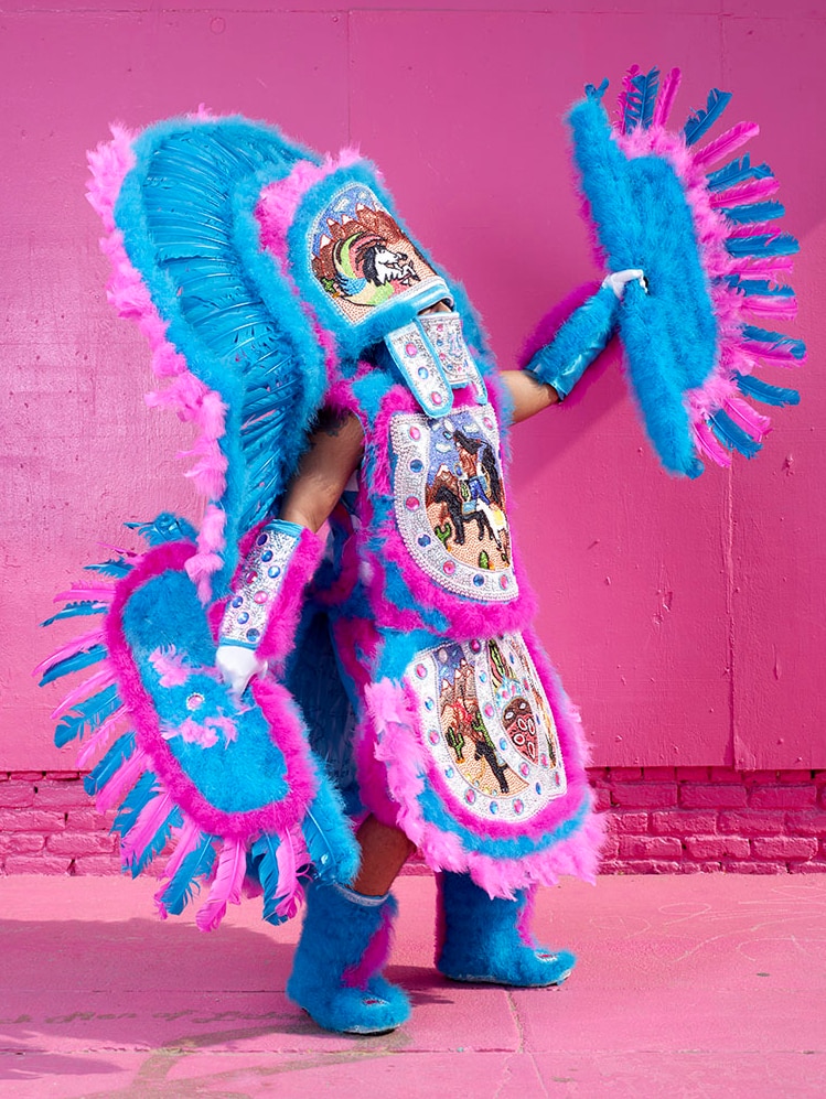 A man adorned in a striking and brightly-coloured blue and pink ceremonial costume