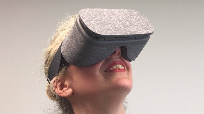 A woman wears a virtual reality headset and looks upwards with open mouth