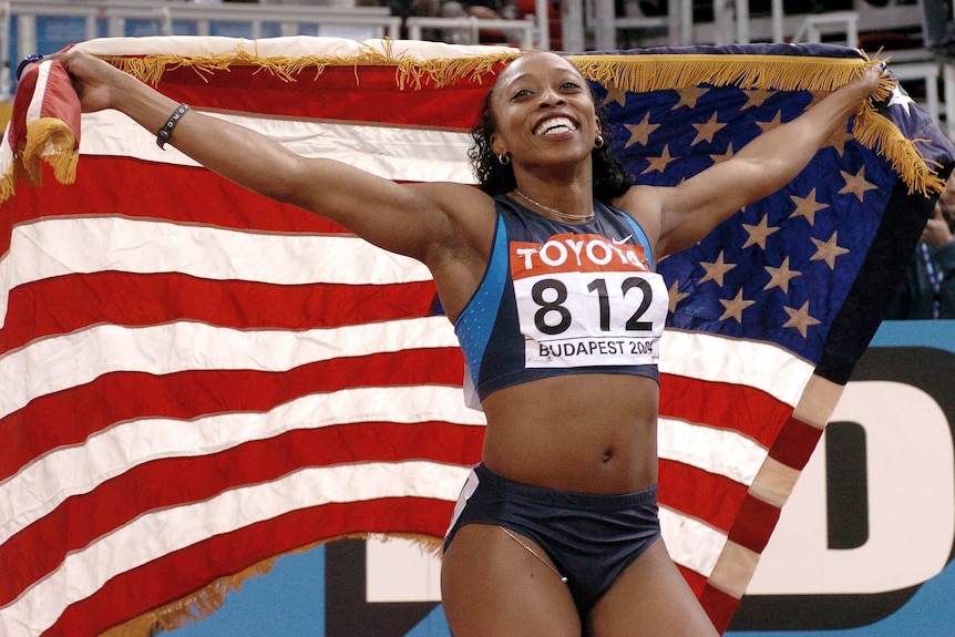 An American female athlete holds the US flag behind her after winning a world indoor title.