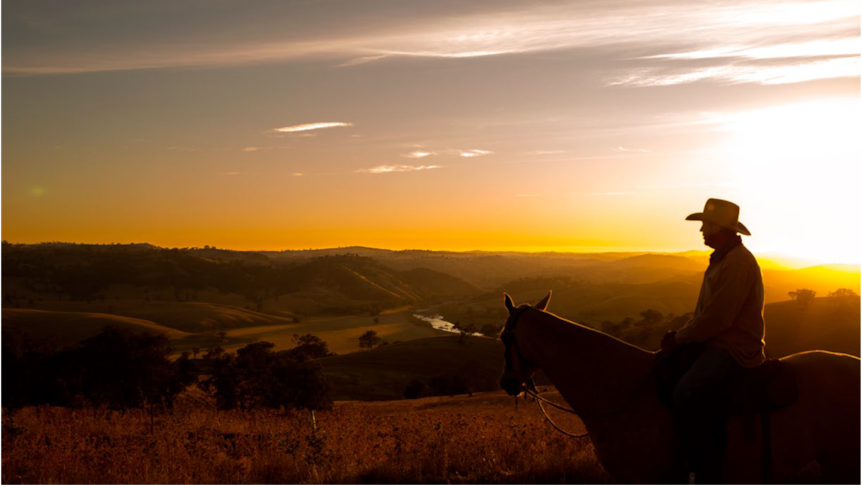 Sunset withthe silhouette of a man in an ukubra on a horse overlooking mountains