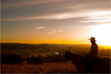 Sunset withthe silhouette of a man in an ukubra on a horse overlooking mountains