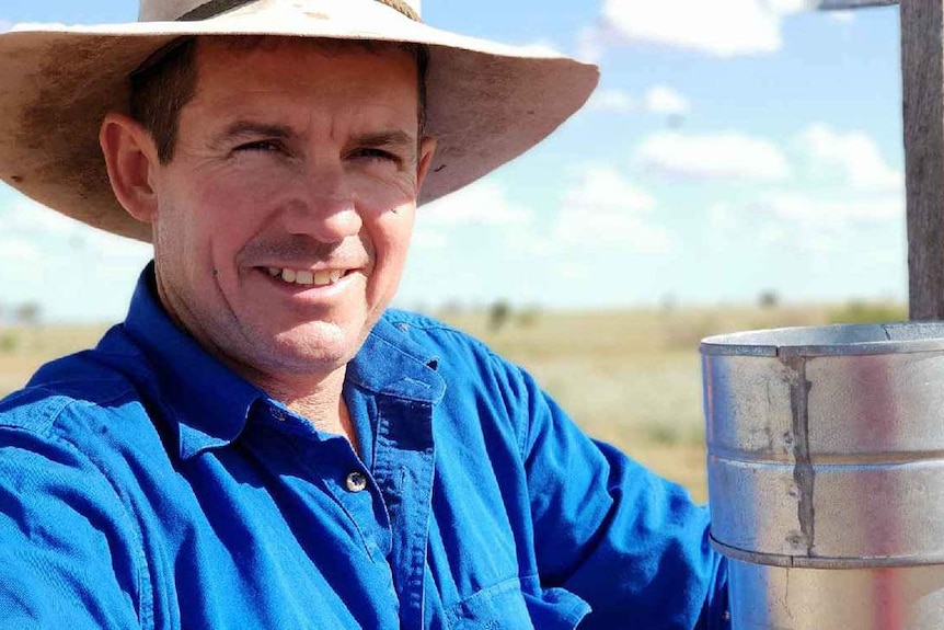 Greg Bowden leans on a fence with a rain gauge at Baratria Station near Longreach in western Queensland.