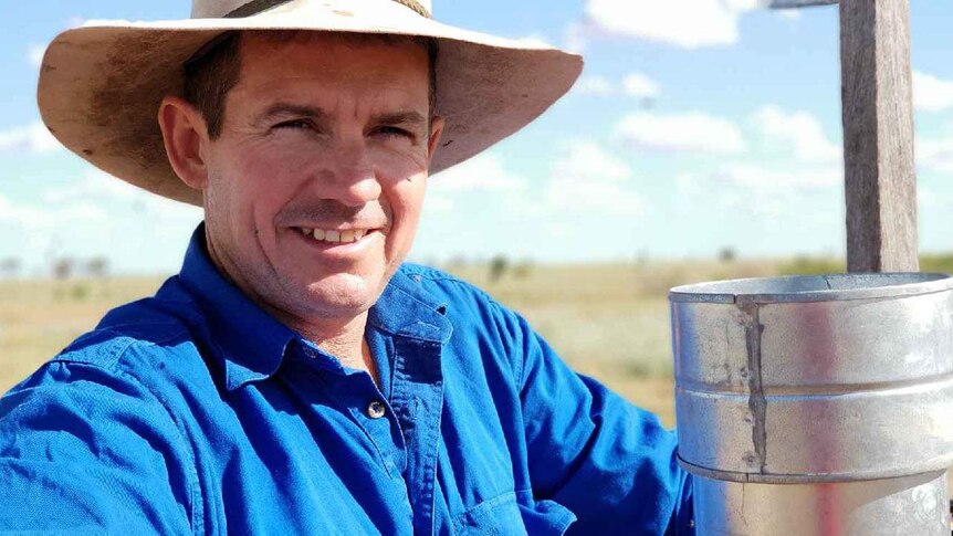 Greg Bowden leans on a fence with a rain gauge at Baratria Station near Longreach in western Queensland.