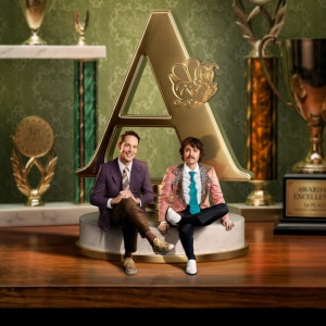 Show artwork for Guy Montgomery's Guy Mont Spelling Bee: Sam Campbell and Guy Montgomery surrounded by awards and trophies