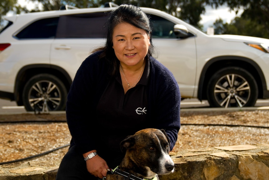 A woman with dark hair squats to pet a dog.