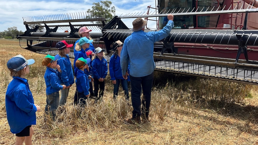 8 students looking at a piece of farming equipment with a farmer
