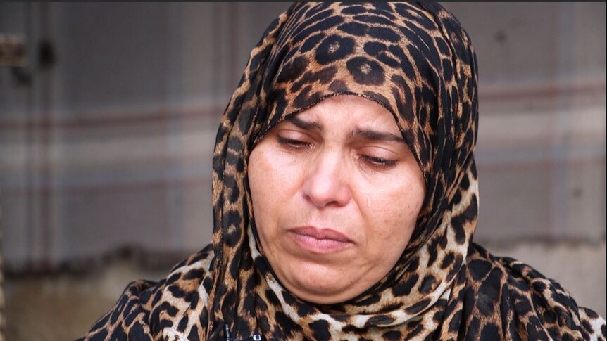 A grieving lady in a leopard print head scarf has tears running down her face.