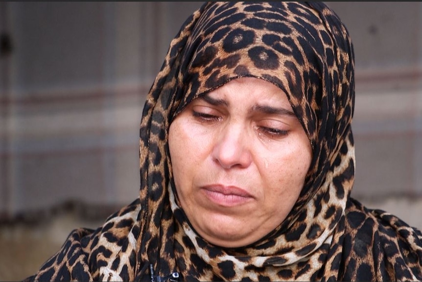 A grieving lady in a leopard print head scarf has tears running down her face.