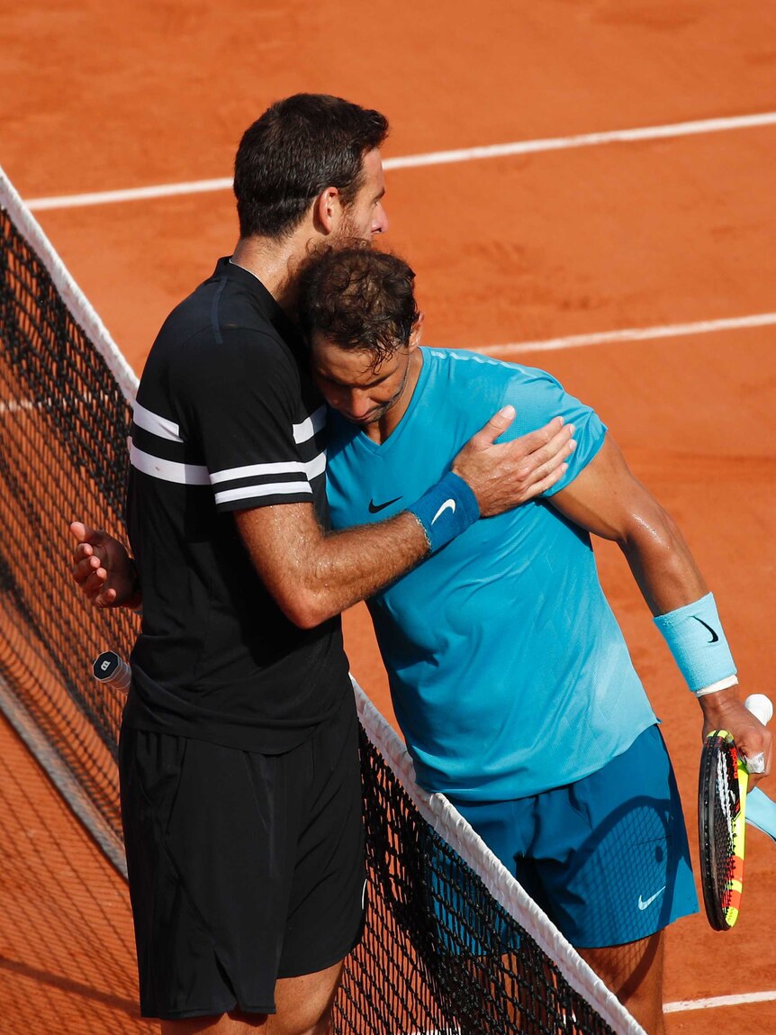 Two men hug over a tennis net.