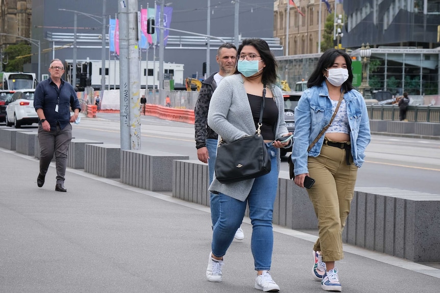 Two women wearing blue surgical masks walking down the street in Melbourne.