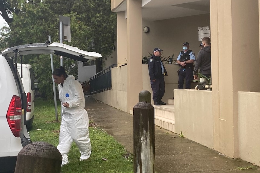 Police stand around together as an investigator looks in a car.