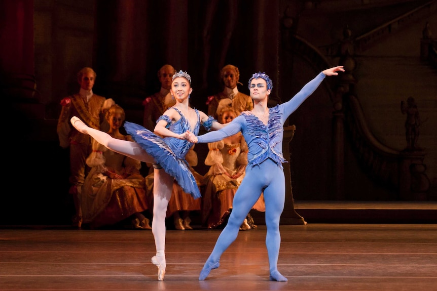 Two dancers, female and male, in blue coloured costumes pose on stage