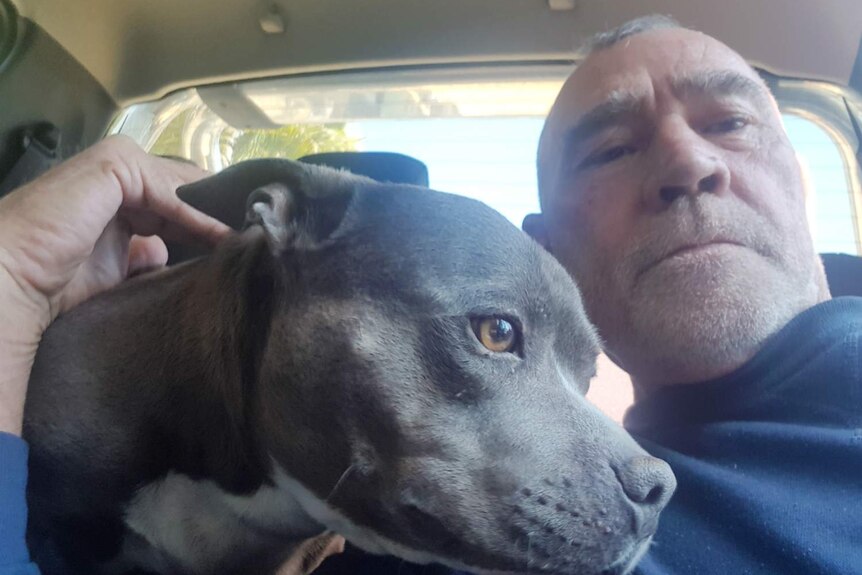 A man looks at the camera, while sitting in a with a dog