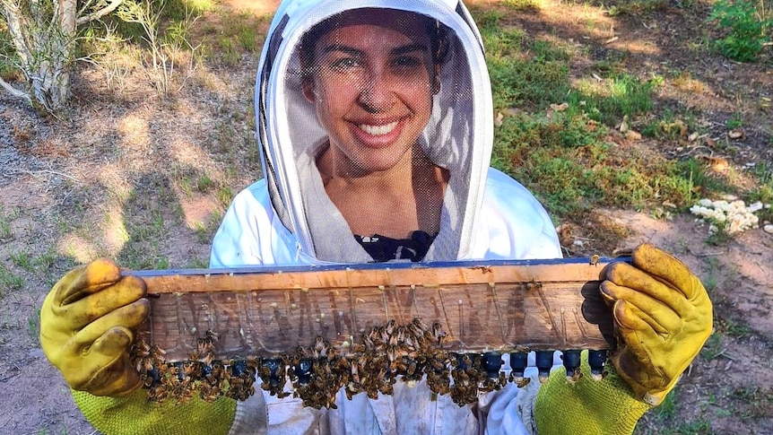An indigenous woman in a bee suit holding a beehive cell