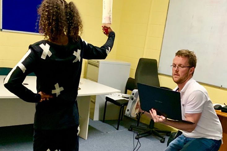 Takoda Johnson stands in a set pose dressed in black with markers with a man scanning her with a computer.