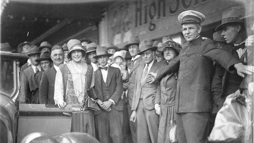 Black and white photo of Beryl Mills surrounded by onlookers.