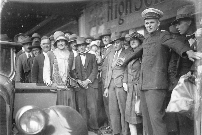 Black and white photo of Beryl Mills surrounded by onlookers.