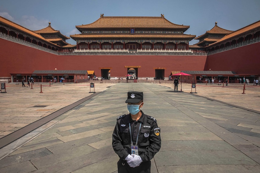 A security guard wearing a face mask and gloves stands at the entrance to Beijing's Forbidden City.