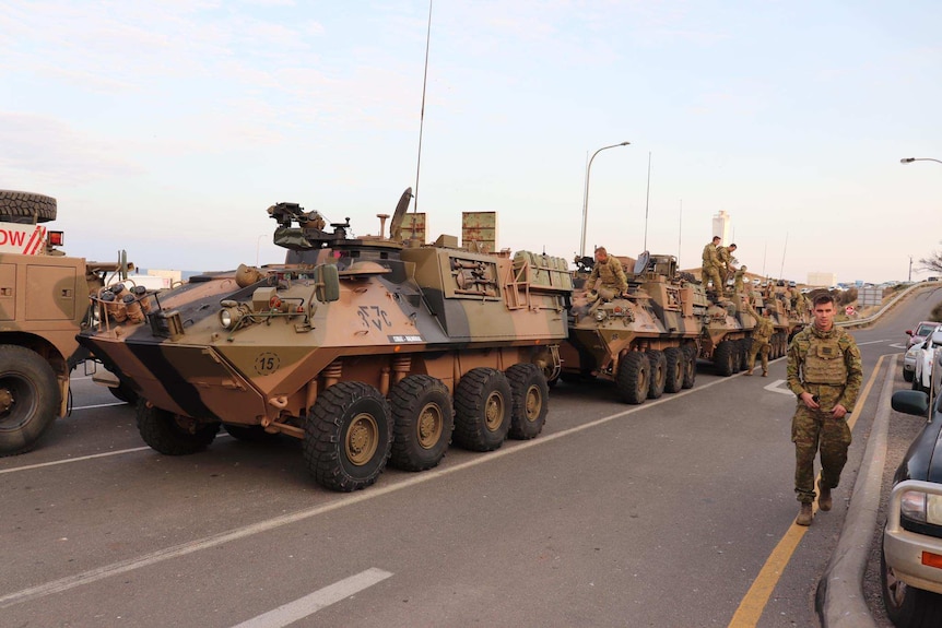 Armoured vehicles in a row with soldiers walking alongside the vehicles