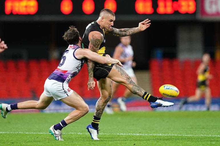 A tattooed AFL player kicks a yellow football.