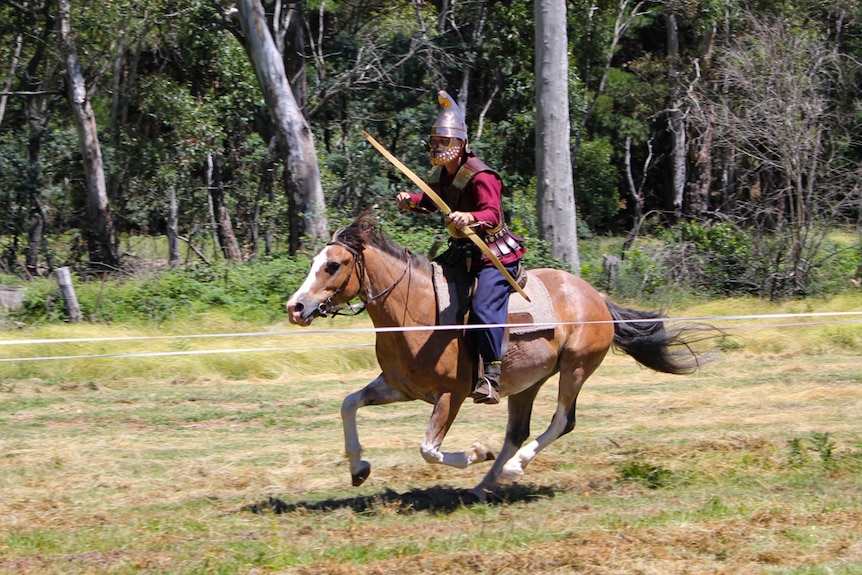 A man wearing armour and carrying a bow and arrow while riding a horse.