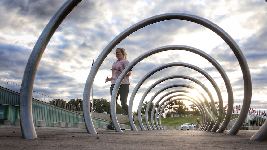 A woman runs behind a bike rack.