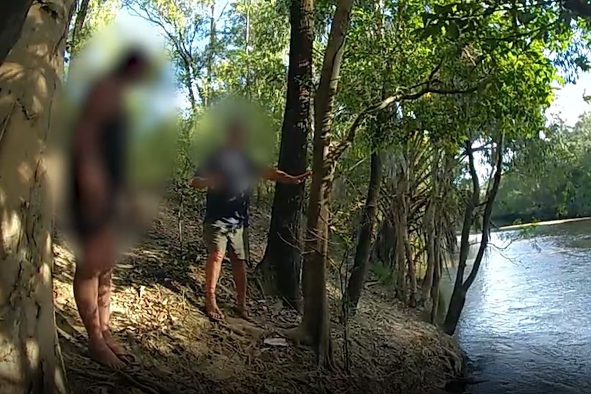 A screenshot of a video showing two blurred men standing on a river bank