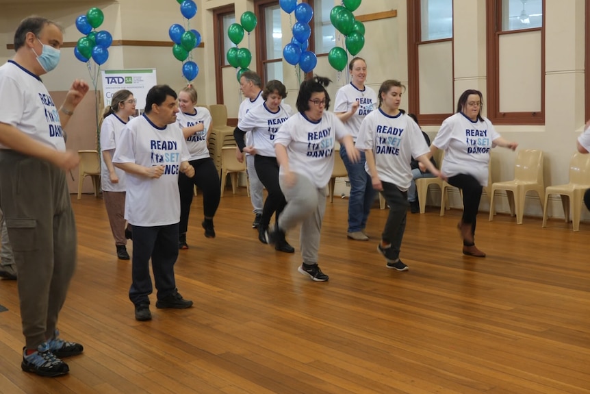 A group of people in a hall, stomping or jumping, with balloons behind them.