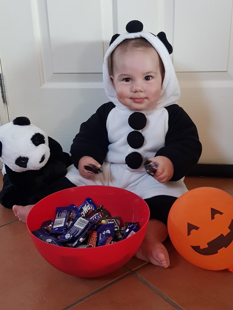 Baby dressed in panda onesie with toy panda and bowl of chocolates