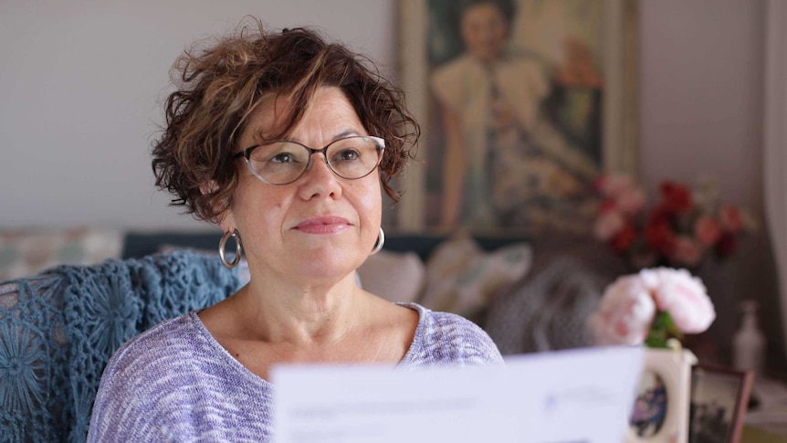 A portrait photo Carol Camilleri holding a piece of paper while looking off to the side of the camera