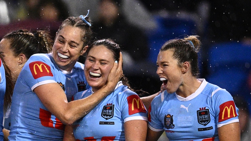 A dozen members of the women's NSW state of origin team smiling and hugging after a try was scored